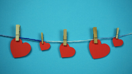 Red hearts with clothespins hanging on rope isolated on blue background. Valentines Day, Healthcare, Mothers Day concept. Copy space