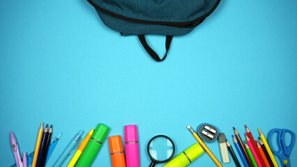 School bag with colorful school supplies on blue background. Back to school concept