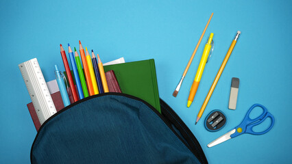 Backpack with school supplies. School supplies look out of a school backpack on a blue background. Blue backpack overflowing with various school supplies