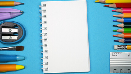 A schoolchild's workplace with an open notebook, pencils, pens, ruler and other stationery on blue background. Back to school concept. Top view. Copy space