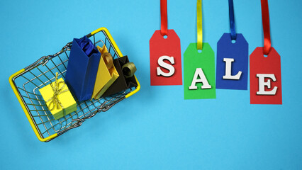 Shopping Cart Full Of Shopping Bags And Gift Boxes On Blue Background. Concept Of Online And Offline Shopping, Sale, Discount