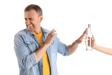 Displeased mature man rejecting bottle of vodka on white background