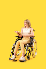 Fototapeta na wymiar Young woman reading book in wheelchair on yellow background