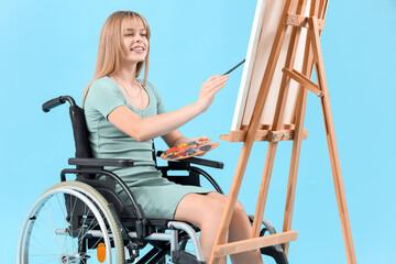 Young woman in wheelchair painting on easel against blue background