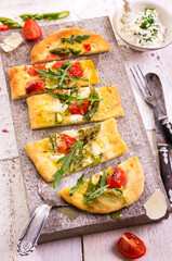 Traditional tarte flambee with green asparagus, tomatoes and mozzarella served as top view on a stone design tray