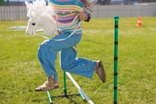 Hobby horsing competition on a green grass, hobby horse riders jumping, equestrian sport training with stick toy horses in a summer sunny day, equipment for hobbihorsing