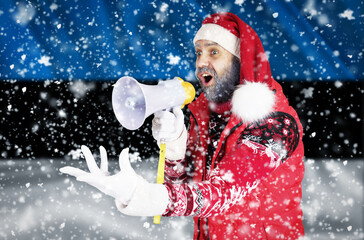 Santa Claus shouts into a megaphone and shows a hand gesture against the background of the flag of Estonia