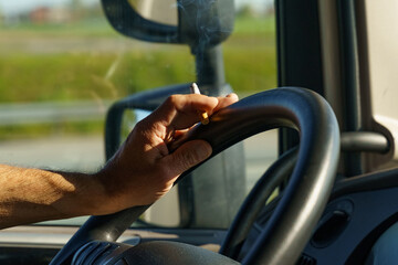 The truck driver holds a smoldering cigarette in his hands and controls the steering wheel of the car at the same time. © Dzmitry