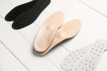 Set of different orthopedic insoles on light wooden background