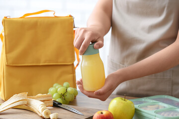 Woman packing bottle of juice into lunch box bag in kitchen