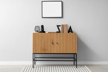 Chest of drawers with books and blank frame on light wall in room