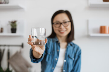 Half-empty glass of water held by chinese woman indoors