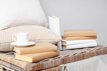 Books with cup and pillows on basket near light wall, closeup