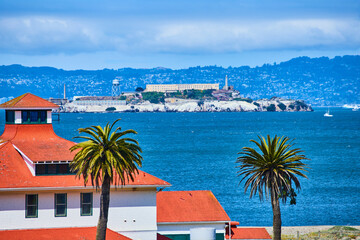 Orange tile roof with palm trees close up and Alcatraz Island in distance with a city on a hill