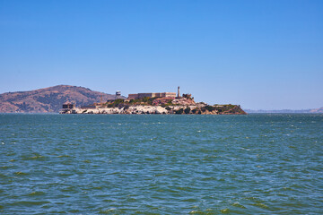 Alcatraz Island on bright summer day with distant mountainous hill and choppy bay waters