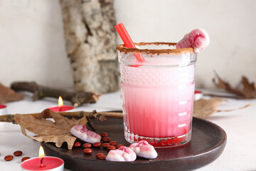 Glass of tasty Margarita cocktail, candles and candies for Halloween on light background
