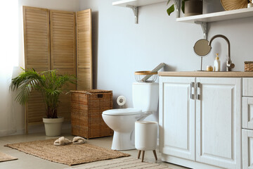 Interior of light restroom with ceramic toilet bowl, sink and vanity cabinets