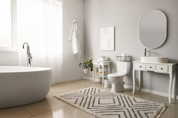 Interior of light restroom with ceramic toilet bowl, bathtub and vanities