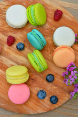 Board with sweet macaroons and berries on wooden background