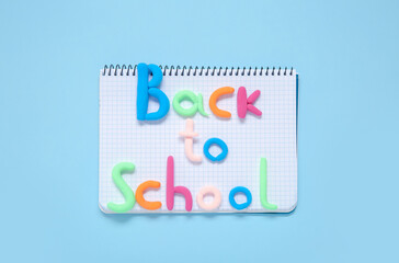 Text BACK TO SCHOOL with notebook on light blue background