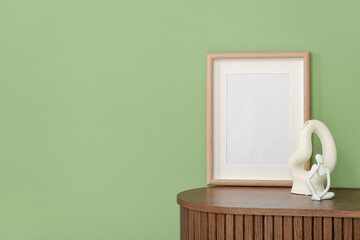 Blank frame and decor on wooden cabinet near green wall, closeup