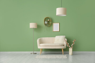 Cozy white sofa with cushion and cotton branches in vase near green wall
