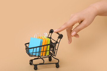 Female hand with small shopping cart on beige background