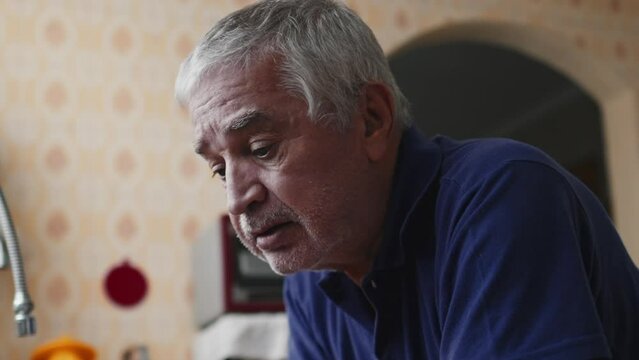 Anxious elderly man struggling with illness leaning on kitchen sink with head looking down struggles with defeat and desperation, dramatic acting