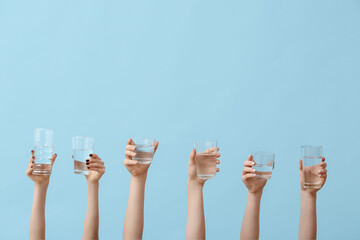 Female hands holding glasses of water on blue background