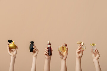 Female hands holding different perfumes on beige background
