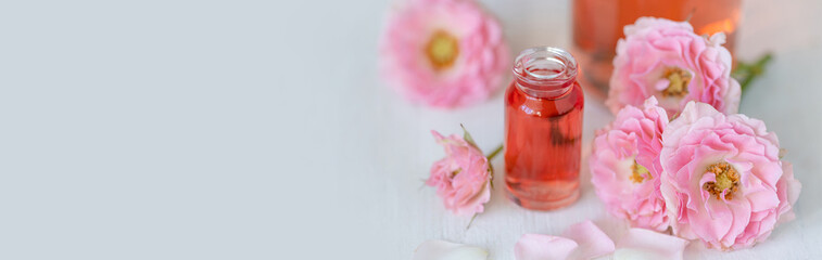 Composition with pure natural organic rose essential oil in glass bottle, luxury perfumery ingredient for fragrance, skin care products, anti-age beauty treatment. Fresh flowers banner copy space text