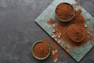 Bowls with cocoa powder and beans on black background