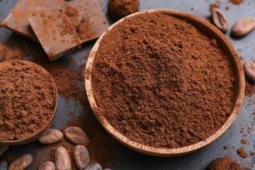 Bowls with cocoa powder, beans and chocolate on black background