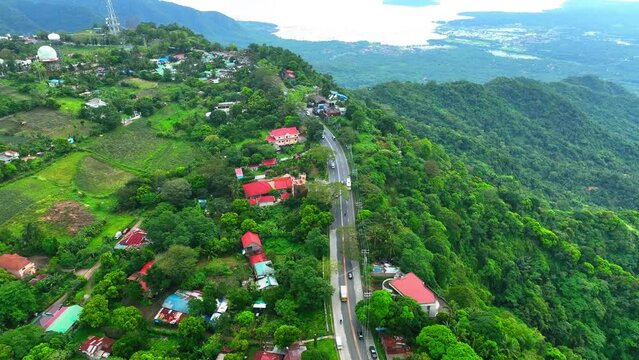 Aerial Tilt Up Shot Of Vehicles On Road Amidst Houses Against Sky, Drone Descending Over City Near Taal Lake - Tagaytay, Philippines