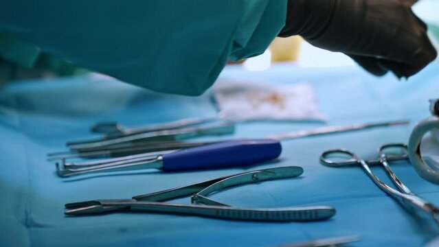 Metal tools on the table prepared for the surgery. Medic's hands in latex gloves take the instruments. Close up.