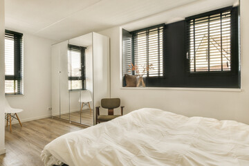 a bedroom with wood flooring and white sheets on the bed, window shutters open to let in natural light