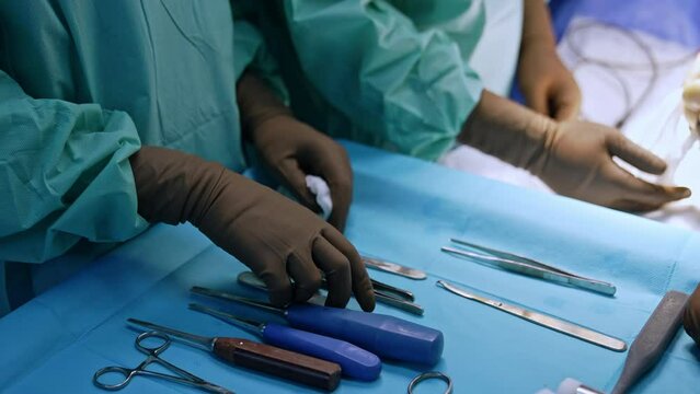 Chisels, forceps and mallet prepared for the orthopedic surgery. Close up. Hands of nurse wearing latex gloves are above the medical tools.