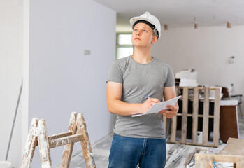Teenage young man in hardhat doing errand in apartment during repair works, checking project...