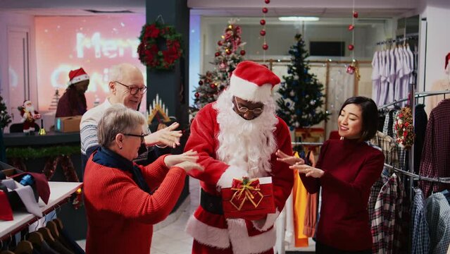 Retail assistant wearing Santa Claus suit in holiday adorn fashion boutique, holding present box acting as raffle tickets container, drawing random senior woman among happy clients