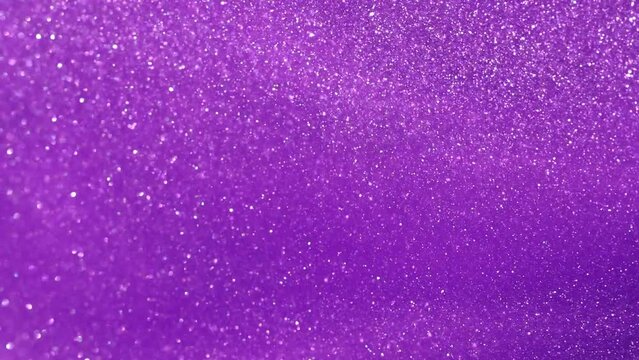 Slow Motion of silvery dust particles floating in purple fluid. Particles dispersion in colored liquid. Abstract glittering background.