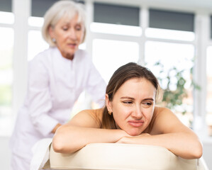 Young female client dissatisfied with work of masseuse in spa salon