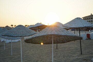 Große runde Sonnenschirme aus Korbgeflecht im Gegenlicht der Abendsonne im Sommer am Strand von...