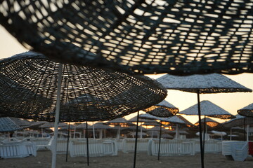 Große runde Sonnenschirme aus Korbgeflecht im Gegenlicht der Abendsonne im Sommer am Strand von...