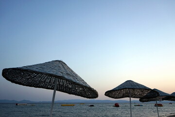 Große runde Sonnenschirme aus Korbgeflecht vor blauem Himmel im Licht der Abendsonne im Sommer am...