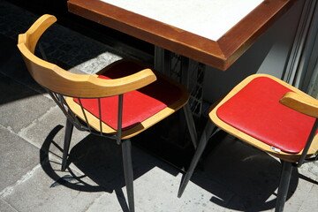 Holztisch mit Stühlen und Kissen in Rot eines Café und Bistro im Sonnenschein mit Licht und...