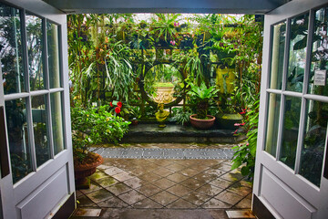 Open white doors leading to moon gate inside trellis covered in plants