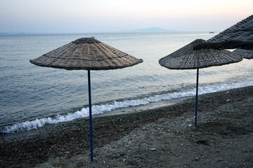 Blick vom Strand in Altinoluk mit Sonnenschirm aus Korbgeflecht im romantischen Licht der untergehenden Sonne auf den Golf von Edremit am Ägäischen Meer in der Provinz Balikesir in der Türkei