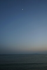 Blick vom Strand in Altinoluk im romantischen Licht der untergehenden Sonne auf den Golf von Edremit mit aufgehendem Mond am Ägäischen Meer in der Provinz Balikesir in der Türkei
