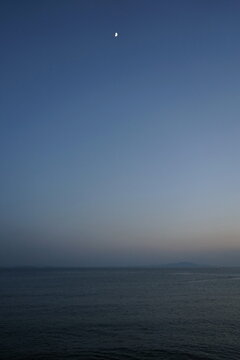 Blick vom Strand in Altinoluk im romantischen Licht der untergehenden Sonne auf den Golf von Edremit mit aufgehendem Mond am Ägäischen Meer in der Provinz Balikesir in der Türkei