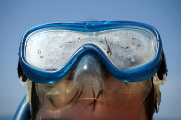 Junge mit blauer Taucherbrille und Schnorchel vor blauem Himmel im Sonnenschein am Strand von...